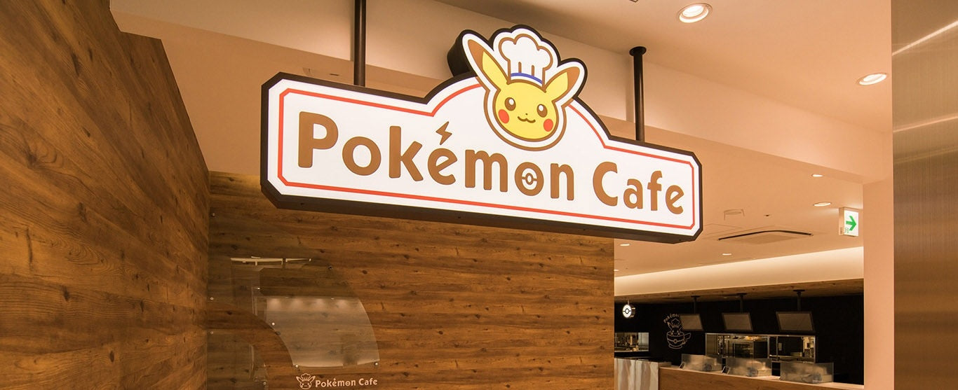 A display of exclusive merchandise from the Pokémon Cafe in Japan. The image features a "Chef Pikachu" plush toy wearing a red hat and apron, alongside a "Waitress Pikachu" plush.